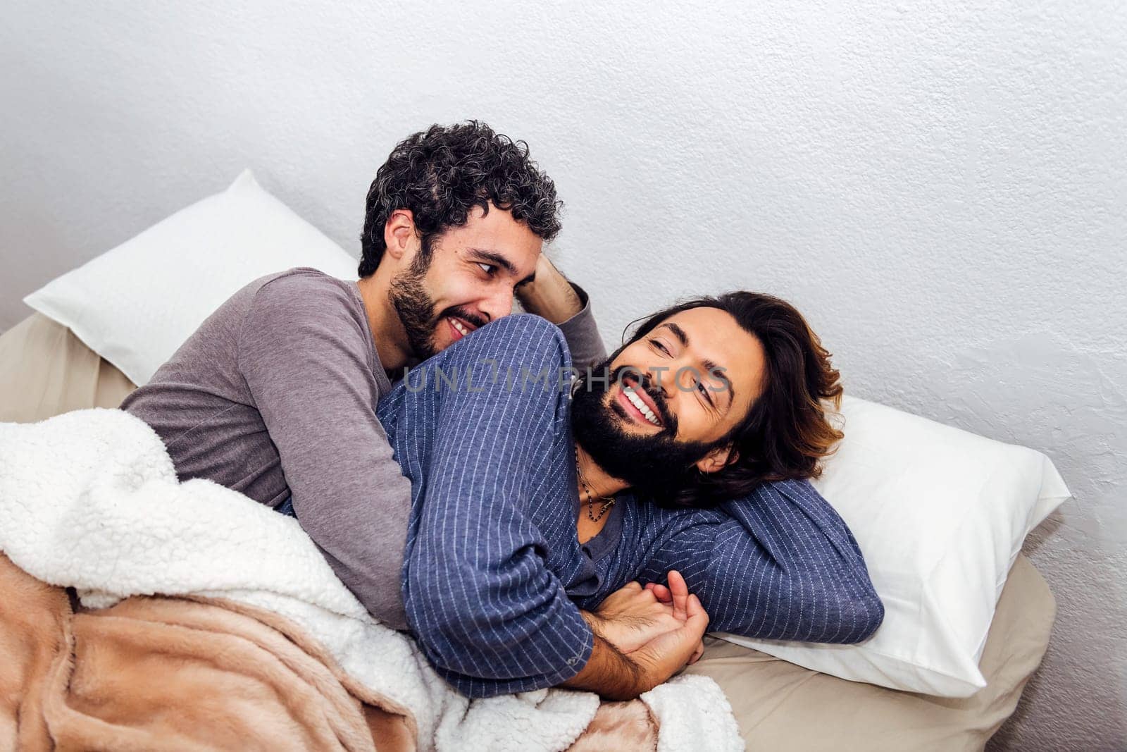 gay male couple cuddling in bed happy to wake up together in the morning, concept of real people lifestyle and love between people of the same sex
