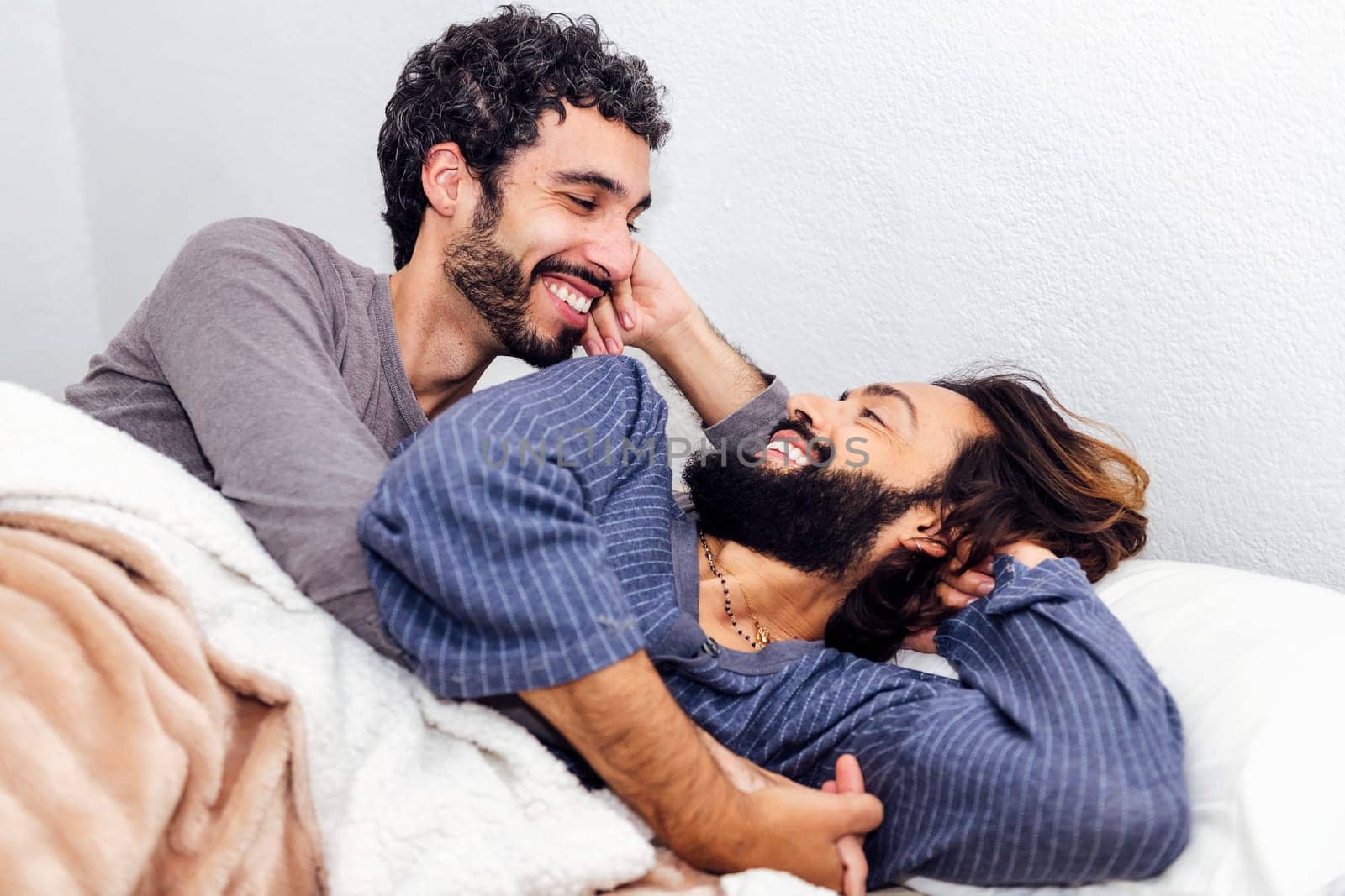 gay male couple in bed smiling happy to wake up together in the morning, concept of real people lifestyle and love between people of the same sex