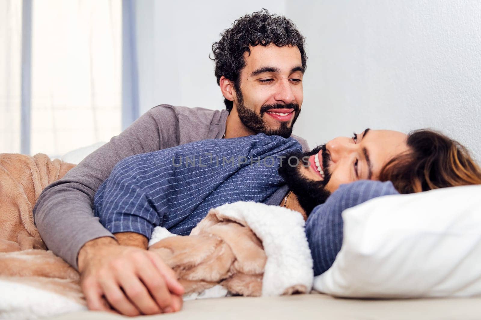 gay male couple in bed smiling happy to wake up together in the morning, concept of real people lifestyle and love between people of the same sex