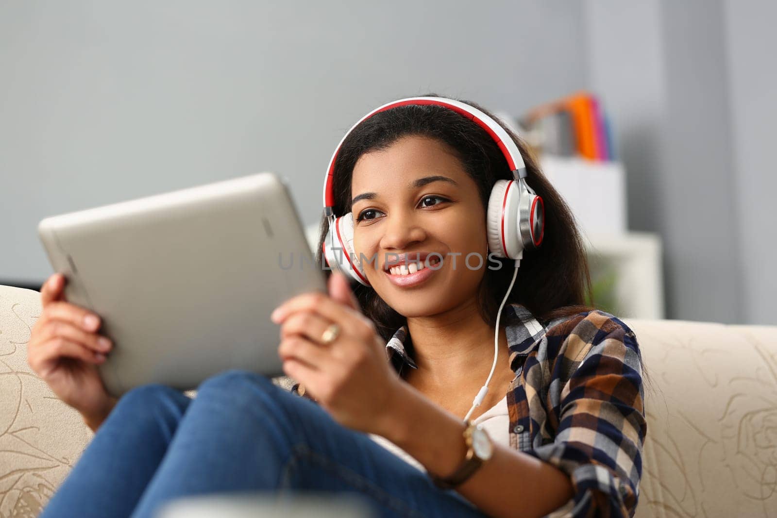 Relaxed charming african american woman in headphones listening to music and choosing with finger on tablet screen by kuprevich