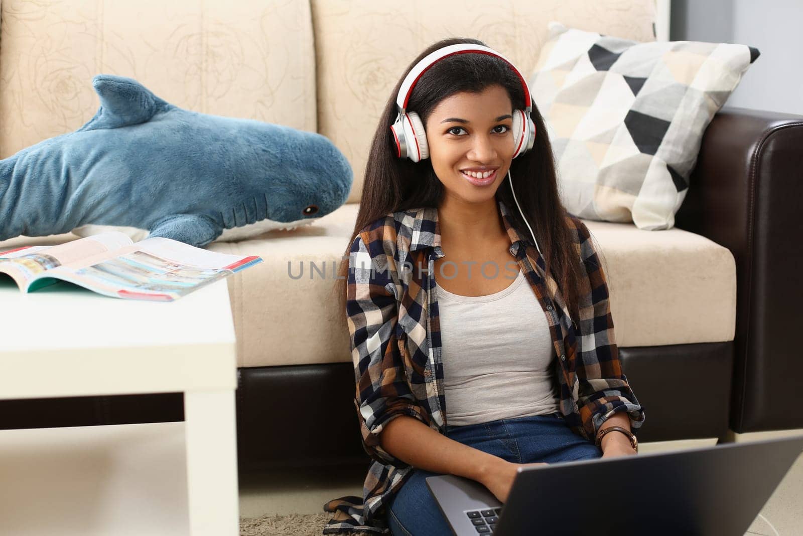 Young beautiful african american woman relaxing and listening to music with headphones on floor. Freelancer working remotely sitting at home with laptop concept