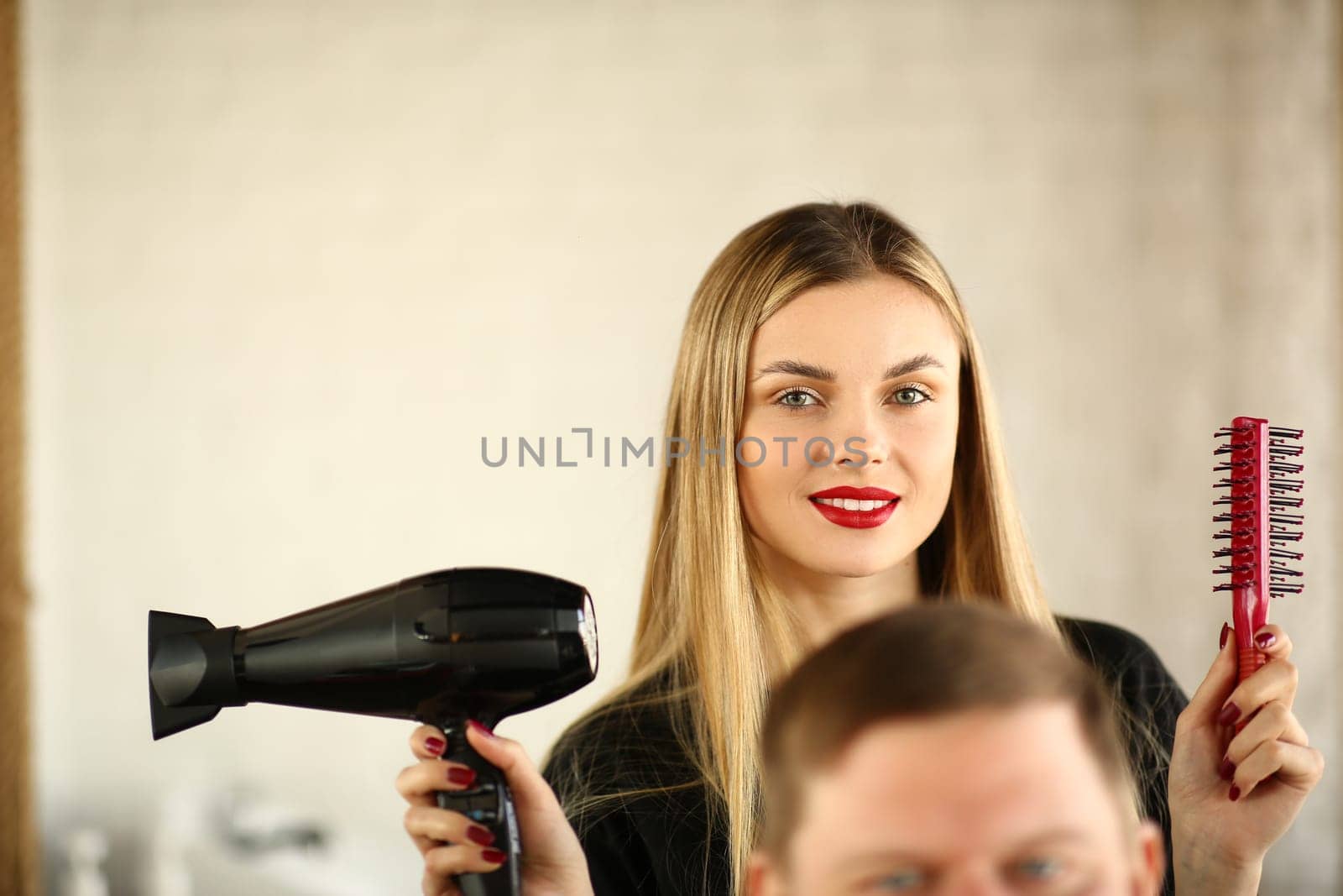 Woman hairdresser is holding hair dryer and comb man is sitting in chair by kuprevich