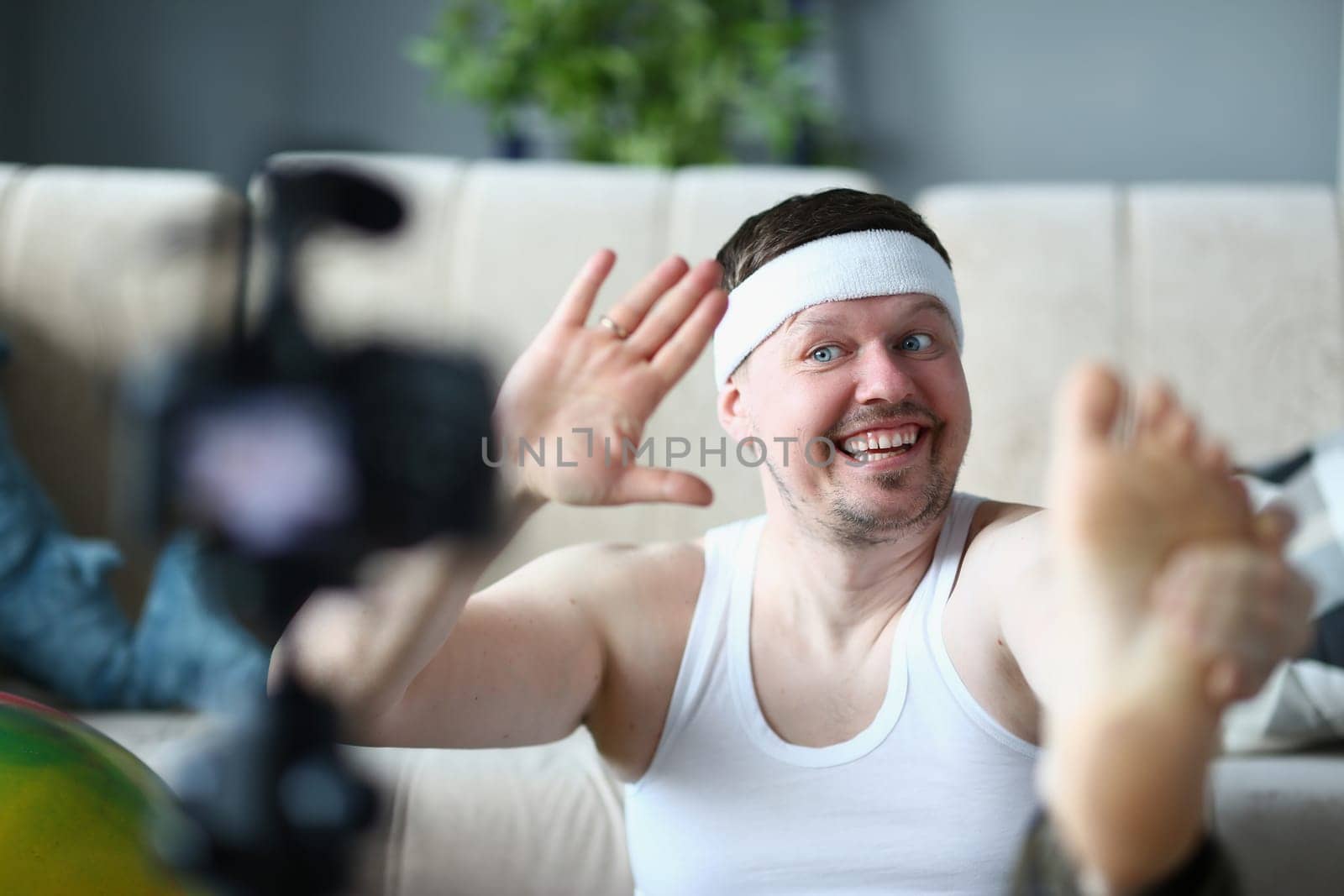 Happy handsome man doing exercises on camera. Shooting a video for sports blog on video camera by kuprevich