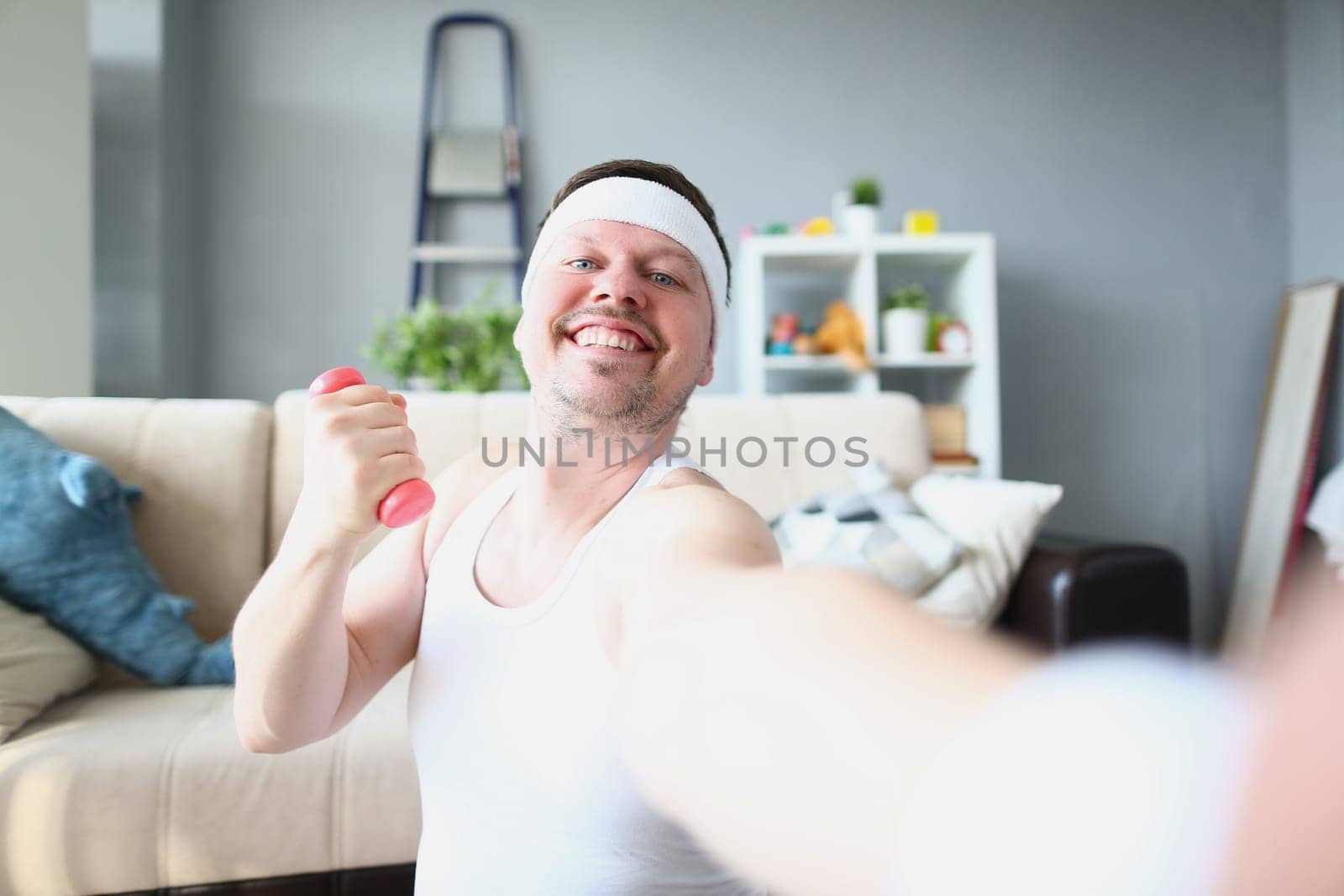 Smiling happy man with dumbbell makes selfie. Home fitness and sports workout blog concept