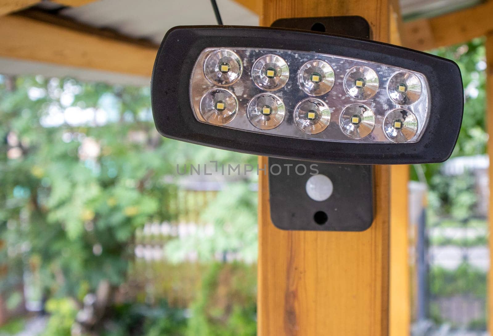 Close-up of an LED spotlight, a spotlight on a wooden post of an open veranda, on a blurred background of the garden. A lantern for lighting the house territory at night.