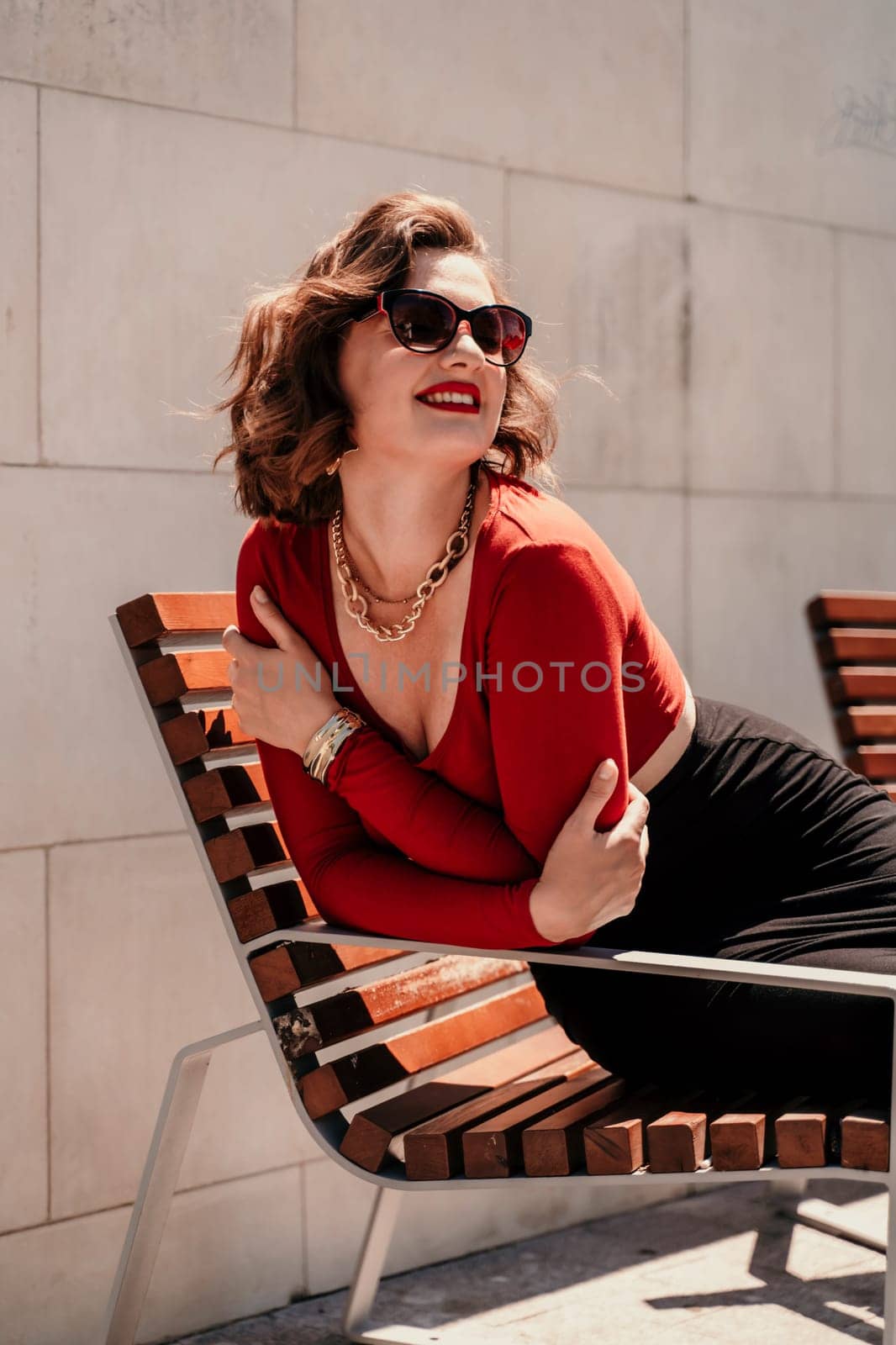 Portrait of a smiling woman on the street. An attractive woman with glasses, a red blouse and a black skirt is sitting on a bench on the street smiling
