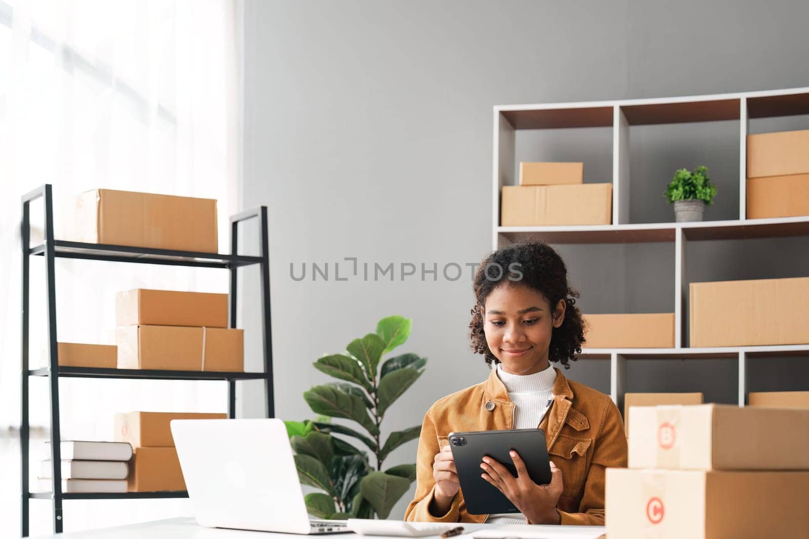 sme business idea. African Americans woman selling online at home with laptop to take orders and to deliver yellow parcel boxes online delivery ideas.