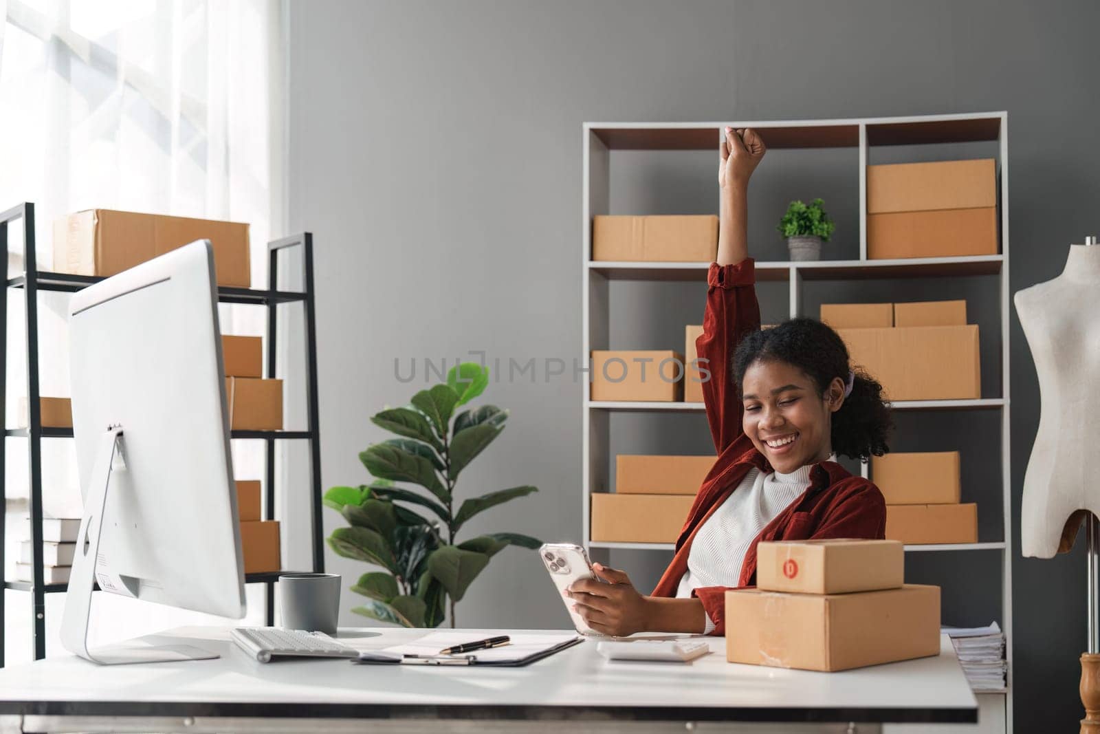 Happy young African Americans woman entrepreneur, Smile for sales success after checking order from online shopping store in a smartphone at home. Concept of merchant business online and e-commerce.