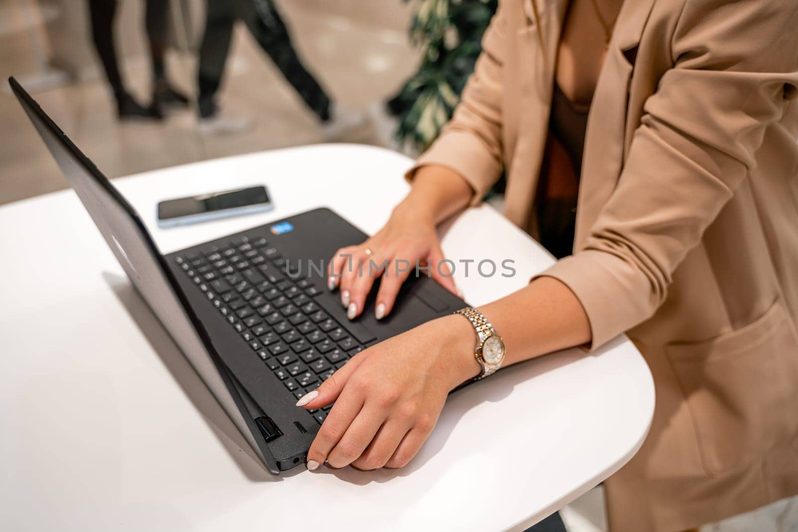 Close-up of beautiful female hands holding a large white cup of cappuccino. A business woman sits in a cafe working at a computer. by Matiunina