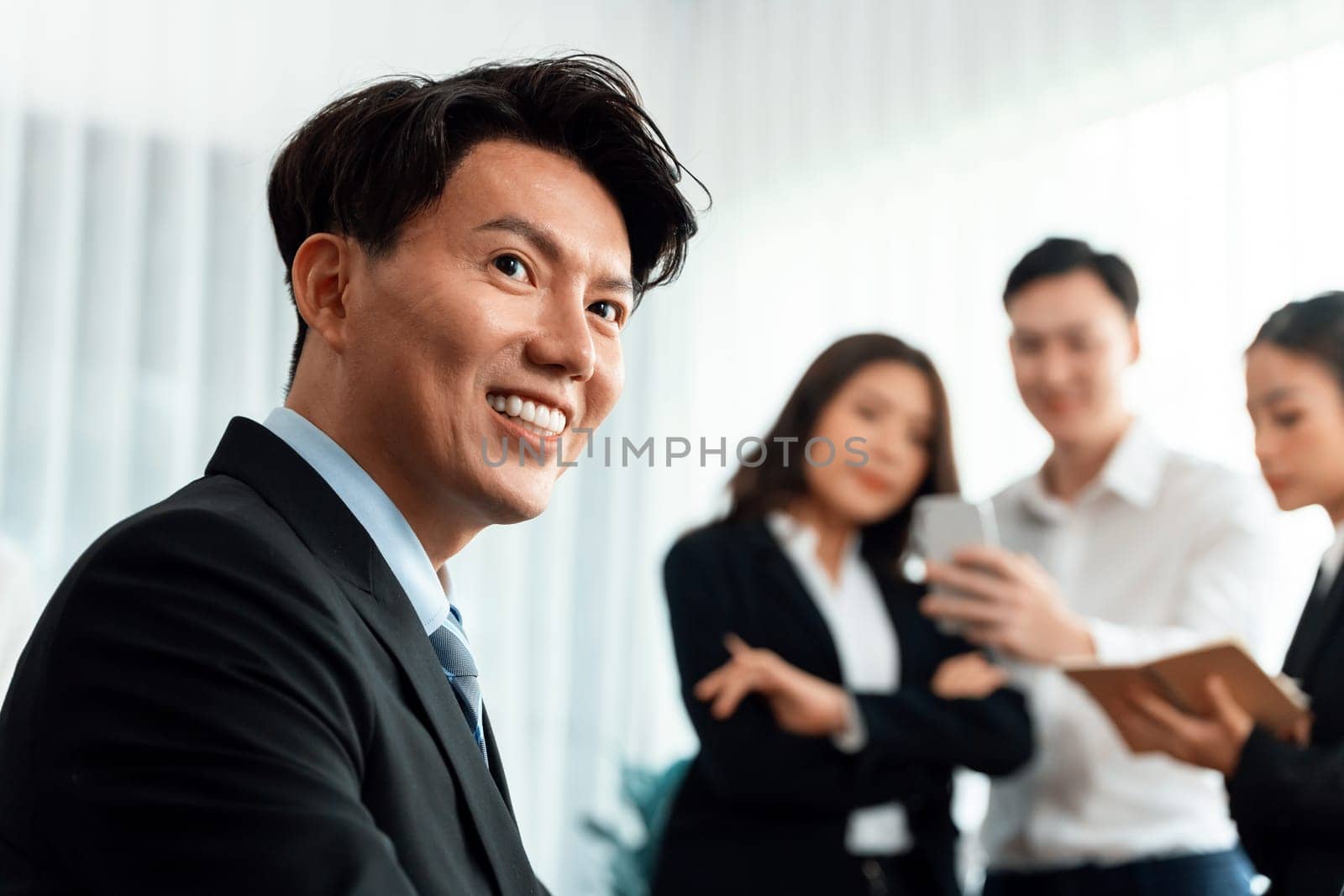 Portrait of focus young successful confident male manager, executive wearing business wear in harmony office arm crossed with blurred meeting background of colleagues, office worker.