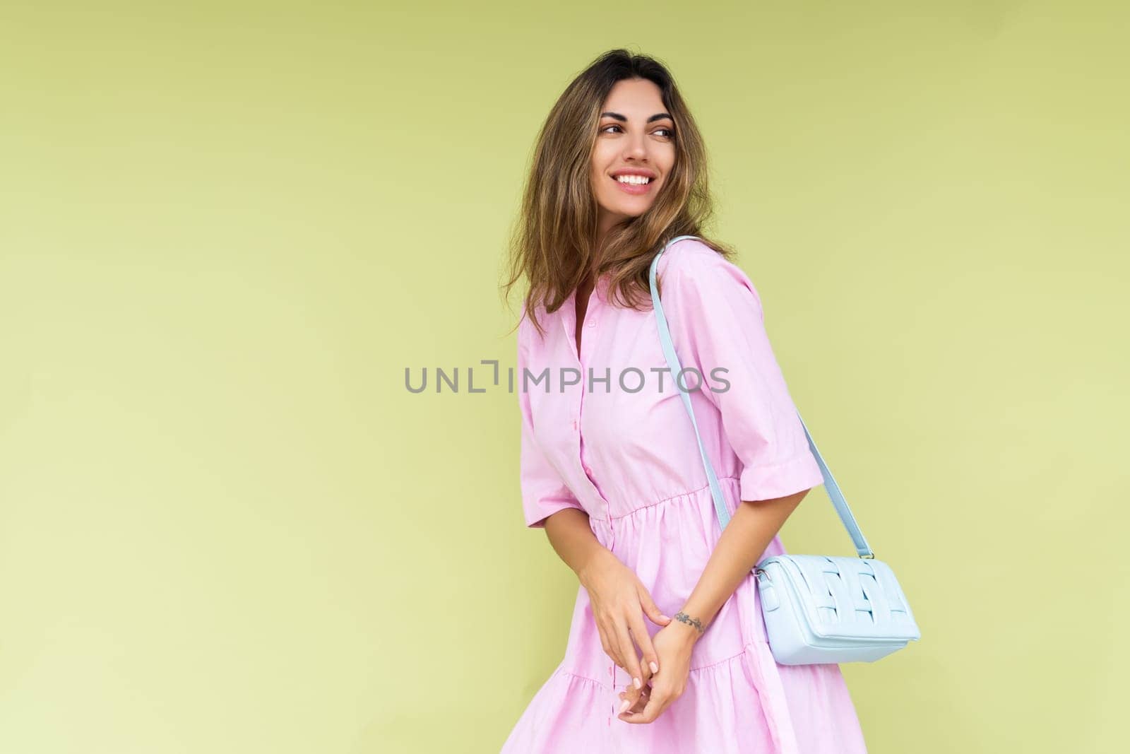 Young woman in casual pink summer cotton dress wear isolated on green background holding cute blue shoulder bag happy big smile