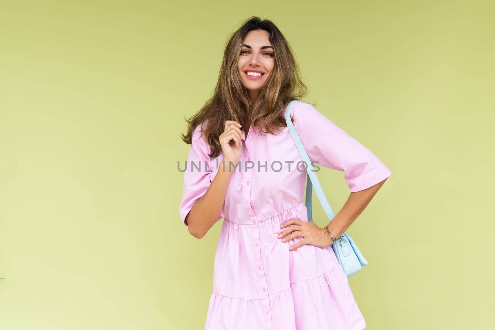 Young woman in casual pink summer cotton dress wear isolated on green background holding cute blue shoulder bag happy big smile