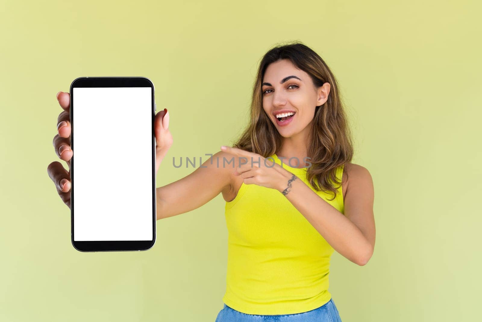 Young woman in casual wear isolated on green background holds a phone with a blank white screen by kroshka_nastya