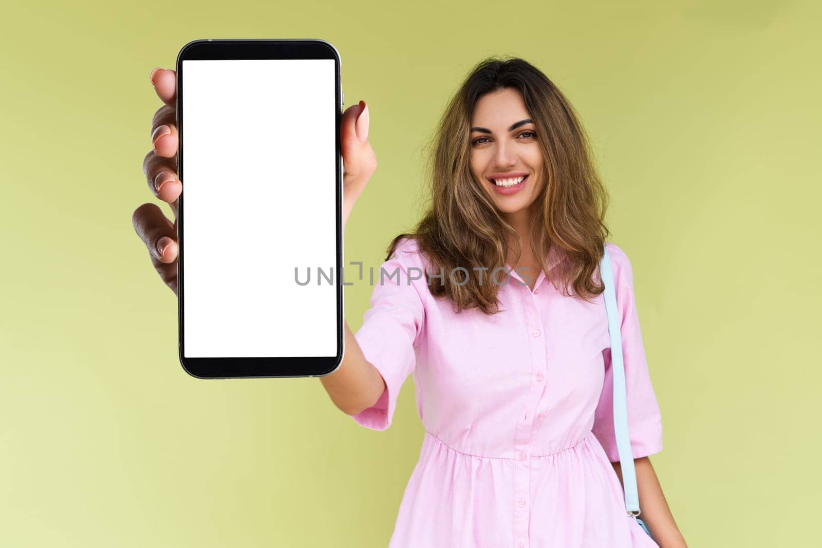 Young woman in casual wear isolated on green background holds a phone with a blank white screen