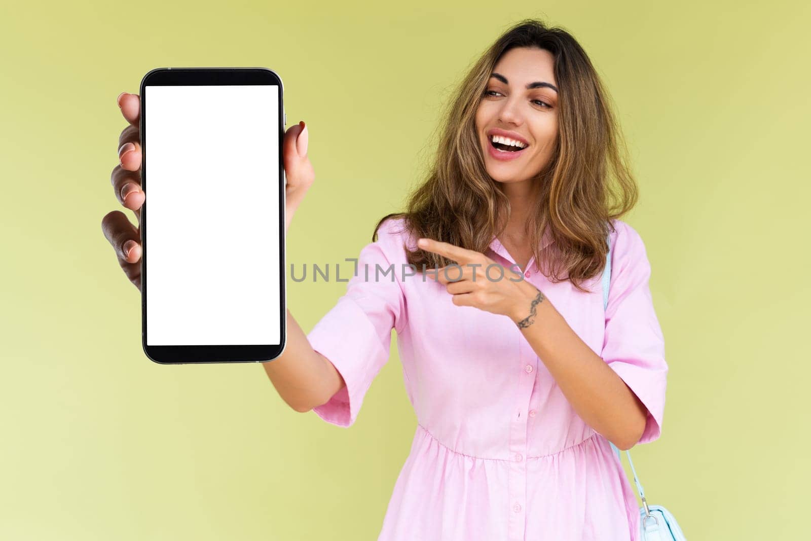 Young woman in casual wear isolated on green background holds a phone with a blank white screen