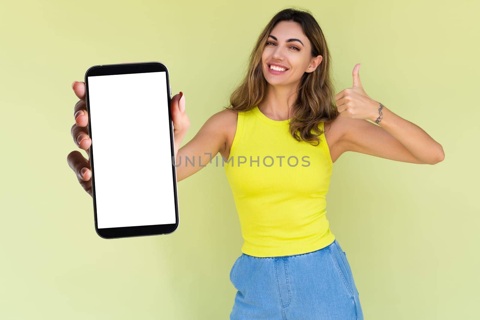 Young woman in casual wear isolated on green background holds a phone with a blank white screen by kroshka_nastya