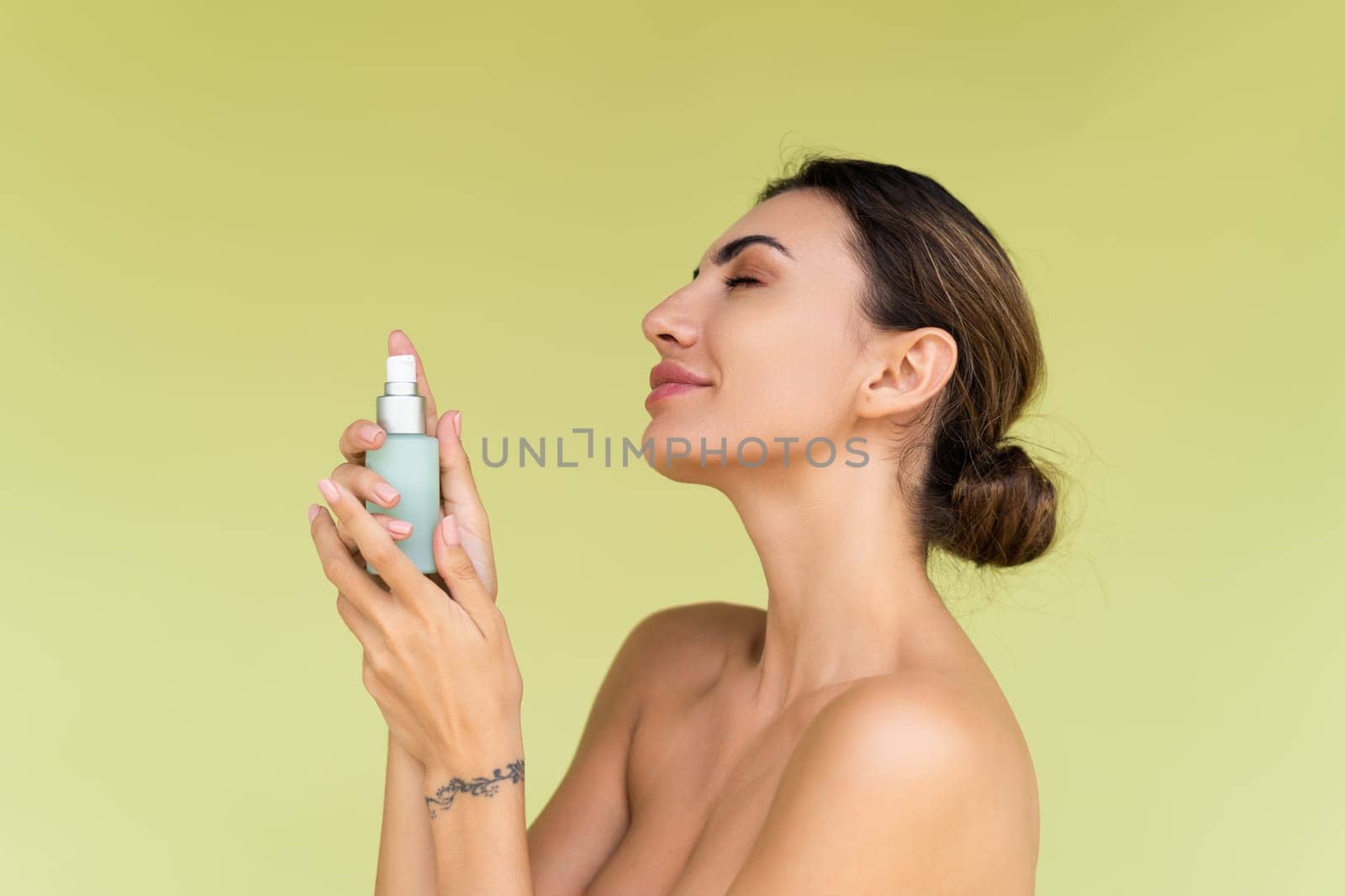 Beauty portrait of young topless woman with bare shoulders on green background with perfect skin and natural makeup holds serum for youth and skin hydration by kroshka_nastya