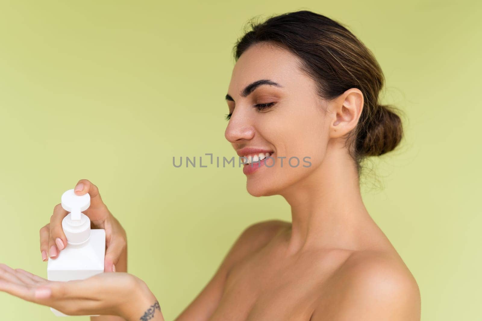 Beauty portrait of young topless woman with bare shoulders on green background with perfect skin and natural makeup holding bottle of shampoo, body lotion by kroshka_nastya