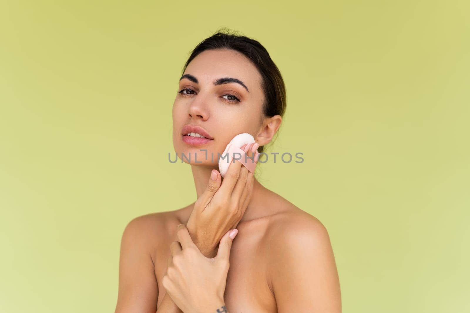 Beauty portrait of young woman with bare shoulders on green background with cosmetic powder puff velour makeup foundation blender sponge applicator by kroshka_nastya