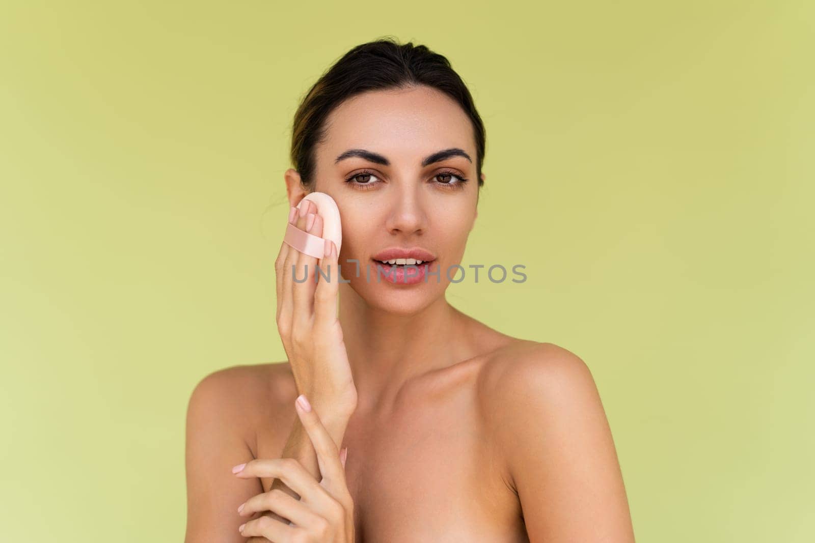 Beauty portrait of young woman with bare shoulders on green background with cosmetic powder puff velour makeup foundation blender sponge applicator by kroshka_nastya