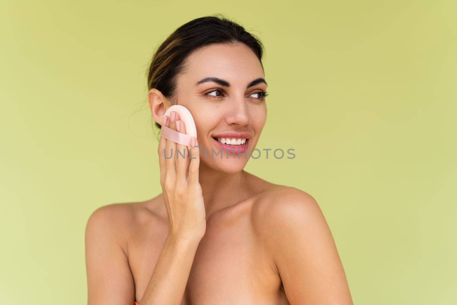 Beauty portrait of young woman with bare shoulders on green background with cosmetic powder puff velour makeup foundation blender sponge applicator by kroshka_nastya