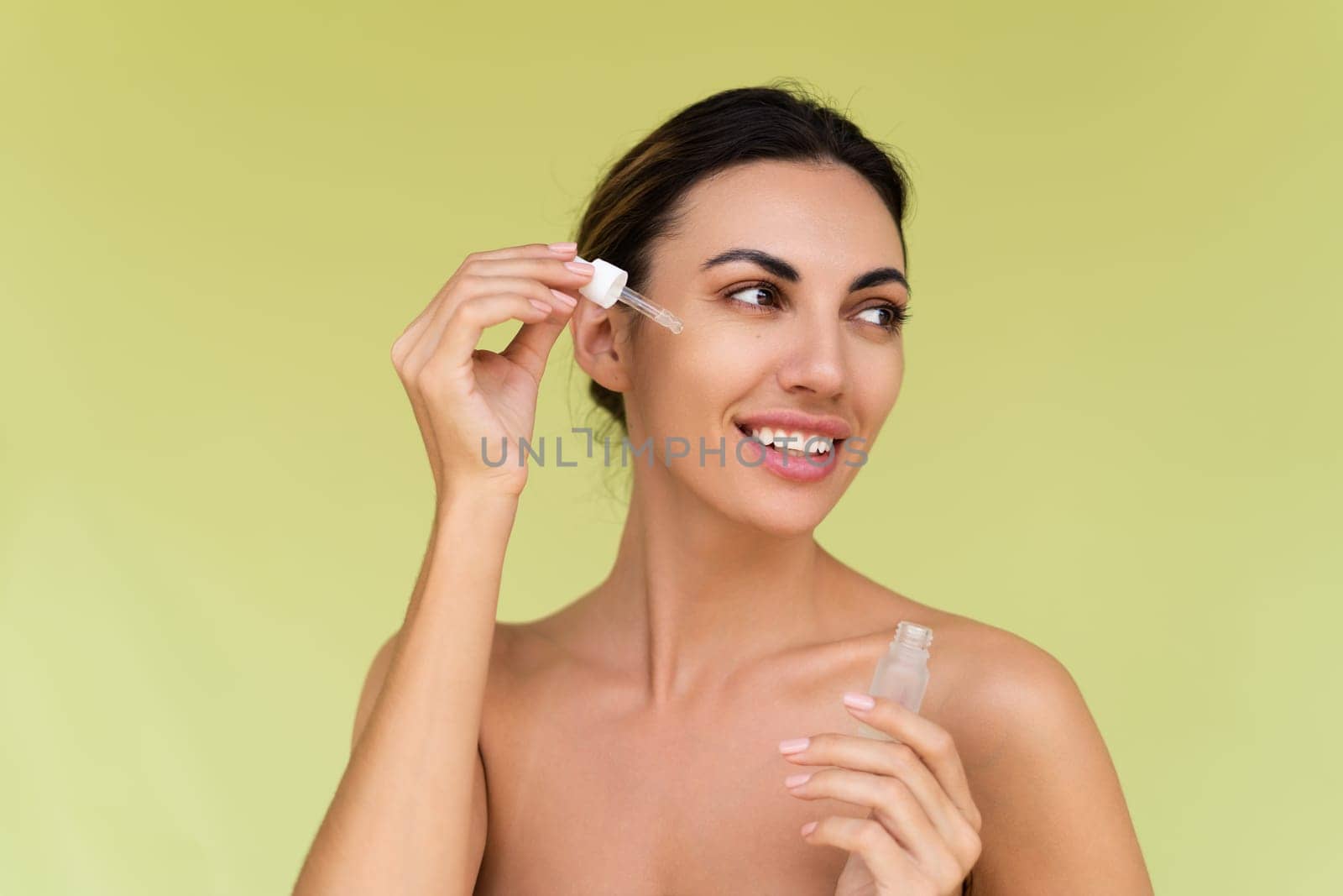 Beauty portrait of young topless woman with bare shoulders on green background with perfect skin and natural makeup holds serum for youth and skin hydration by kroshka_nastya