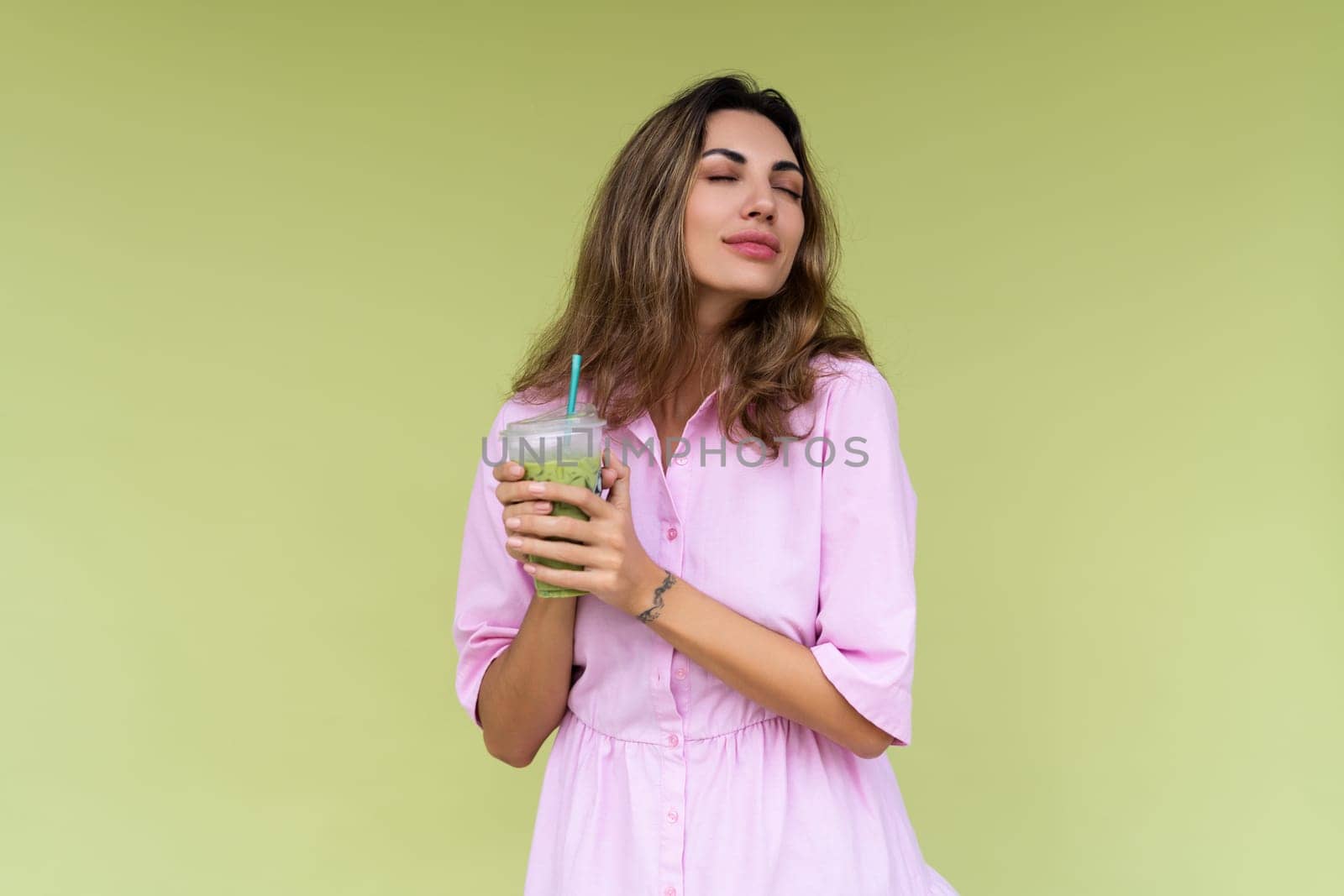 Young woman in casual wear isolated on green background positive vibes enjoying fresh ice green matcha tea with milk at hot summer day