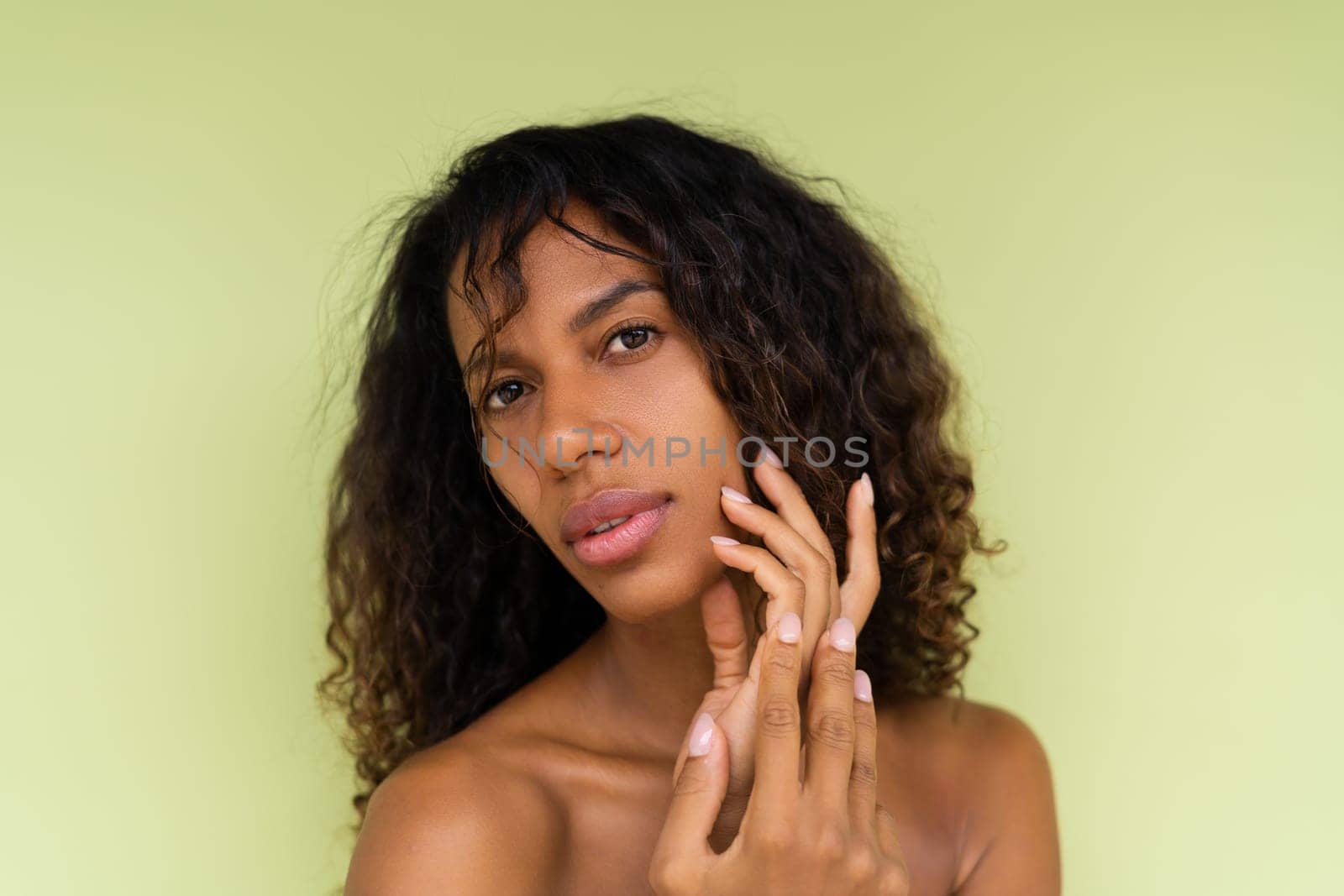 Beauty portrait of young topless african american woman with bare shoulders on green background with perfect skin and natural makeup