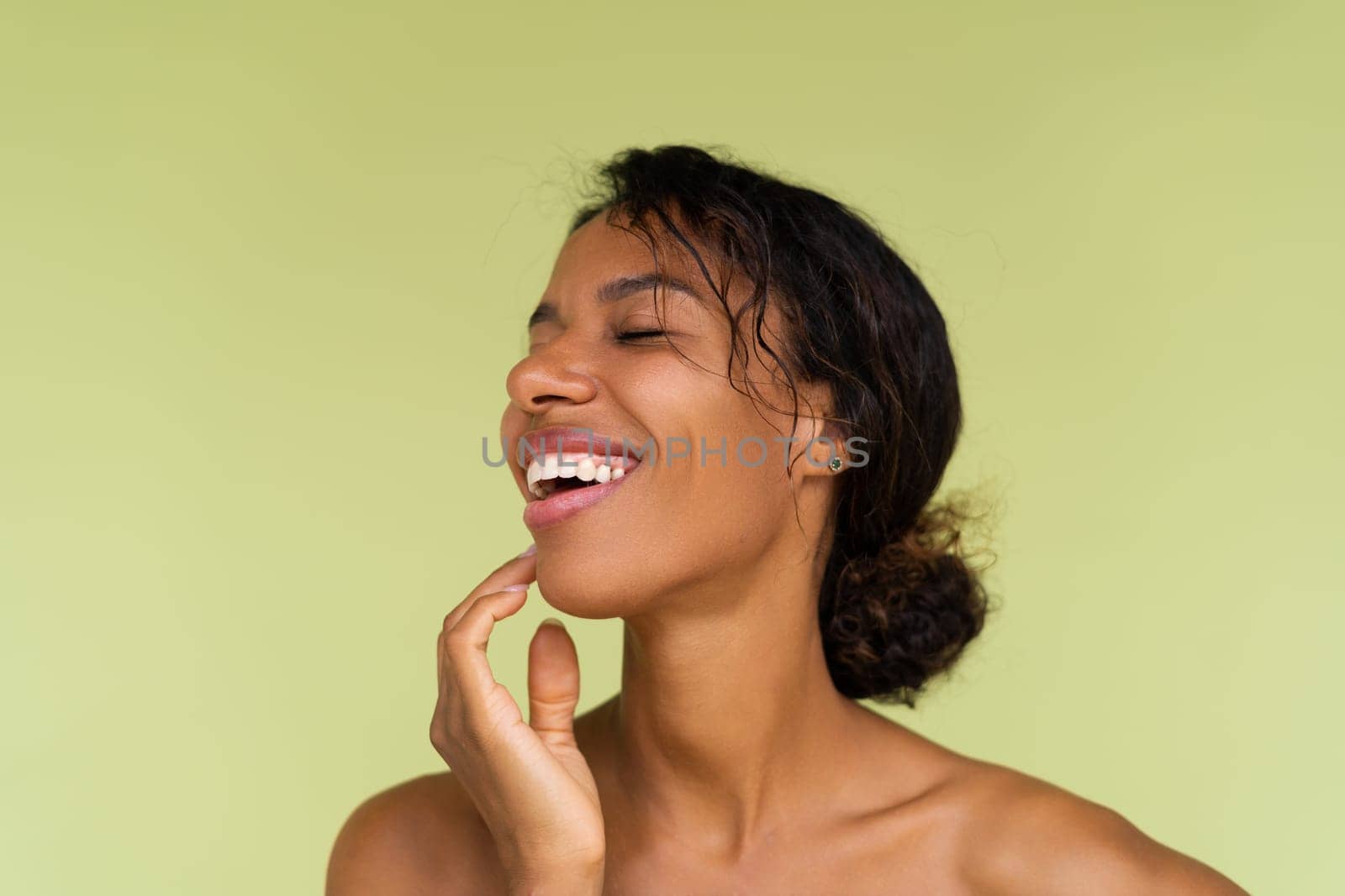 Beauty portrait of young topless african american woman with bare shoulders on green background with perfect skin and natural makeup