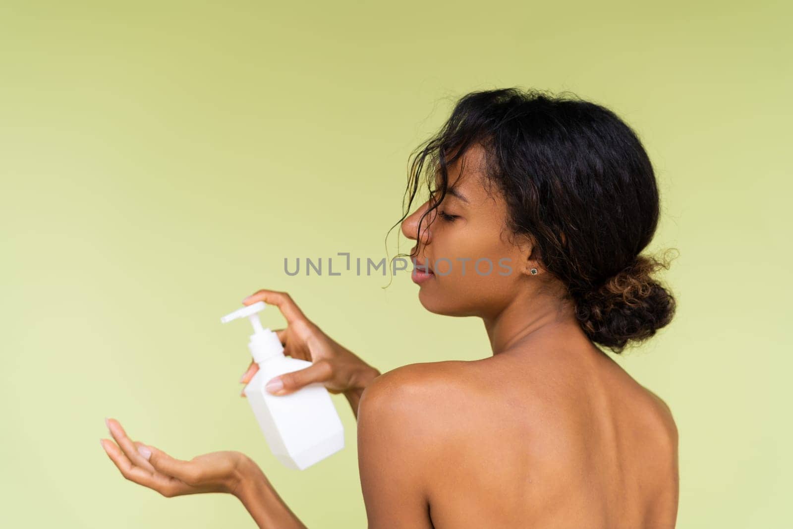 Beauty portrait of young topless african american woman with bare shoulders on green background with white bottle of body lotion by kroshka_nastya