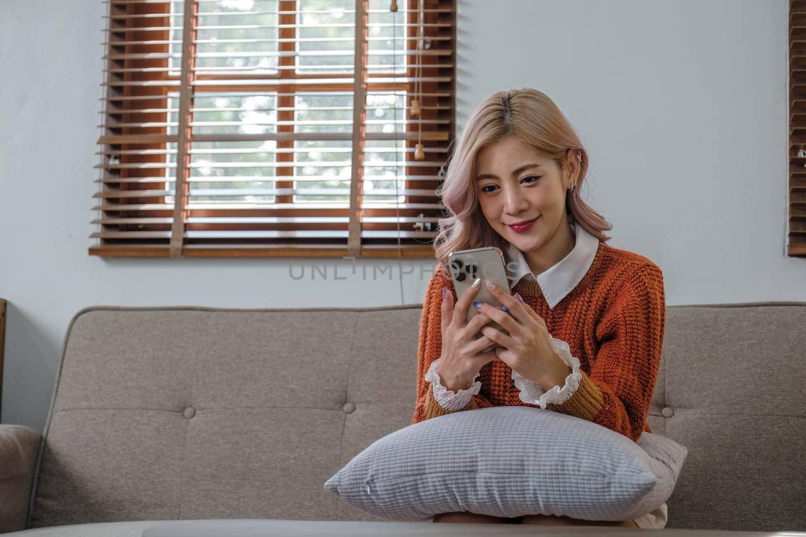 Happy young asian woman relaxing at home. Female is lying down on sofa and using mobile smartphone..