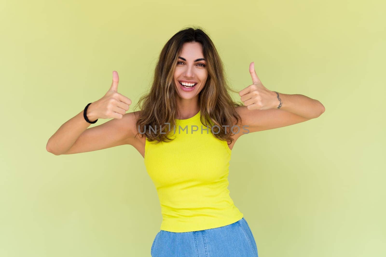 Young brunette in casual wear isolated on green background happy look to camera smile excited showing thumbs up