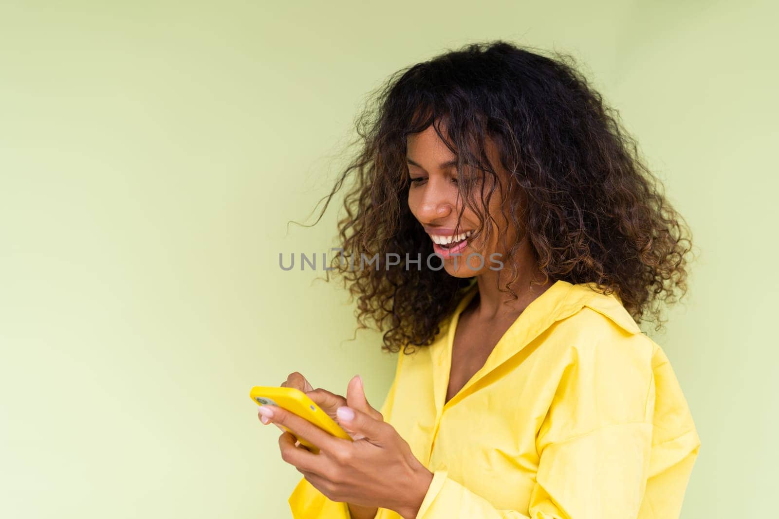 Beautiful african american woman in casual shirt on green background holds mobile phone with a smile by kroshka_nastya