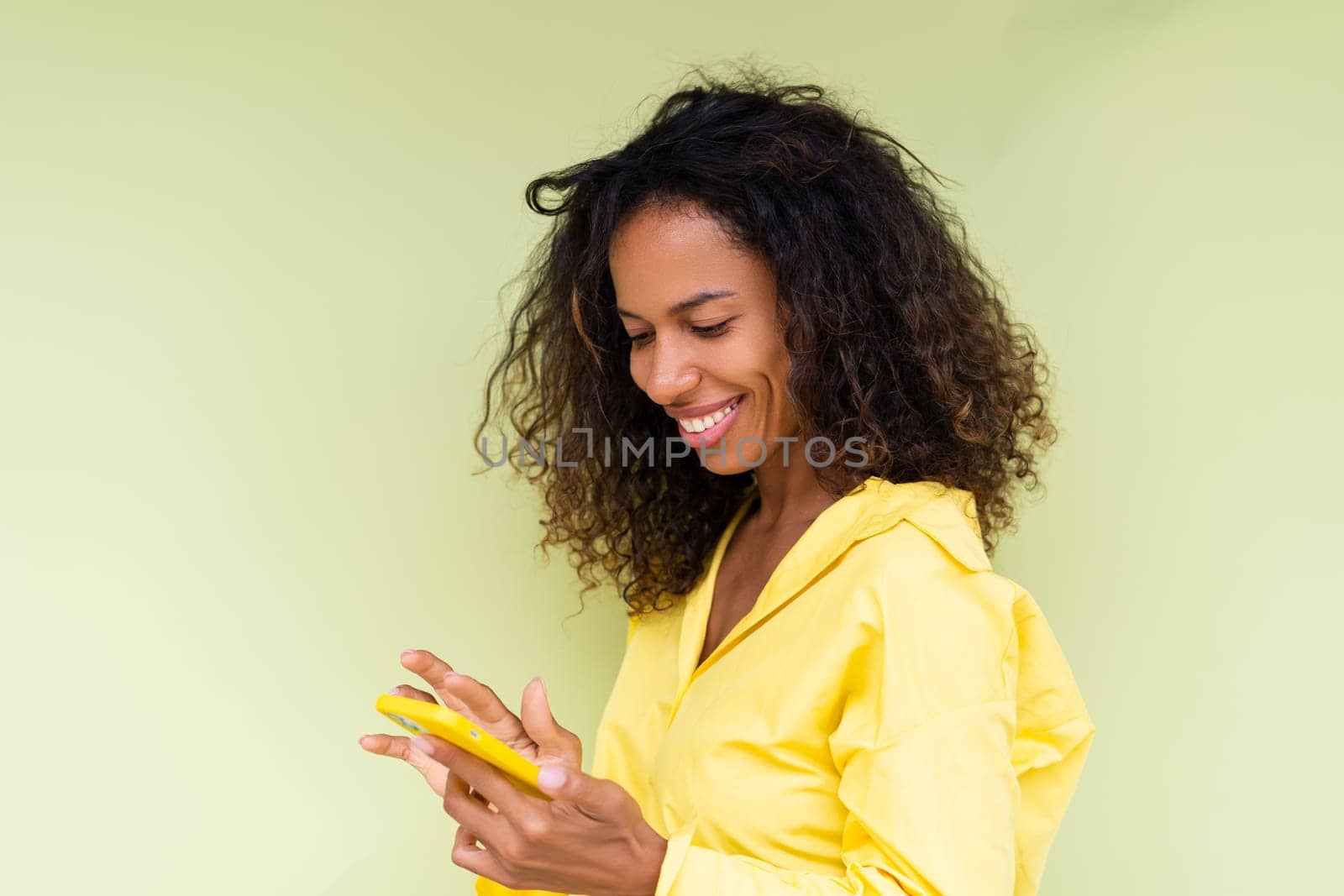 Beautiful african american woman in casual shirt on green background holds mobile phone with a smile by kroshka_nastya