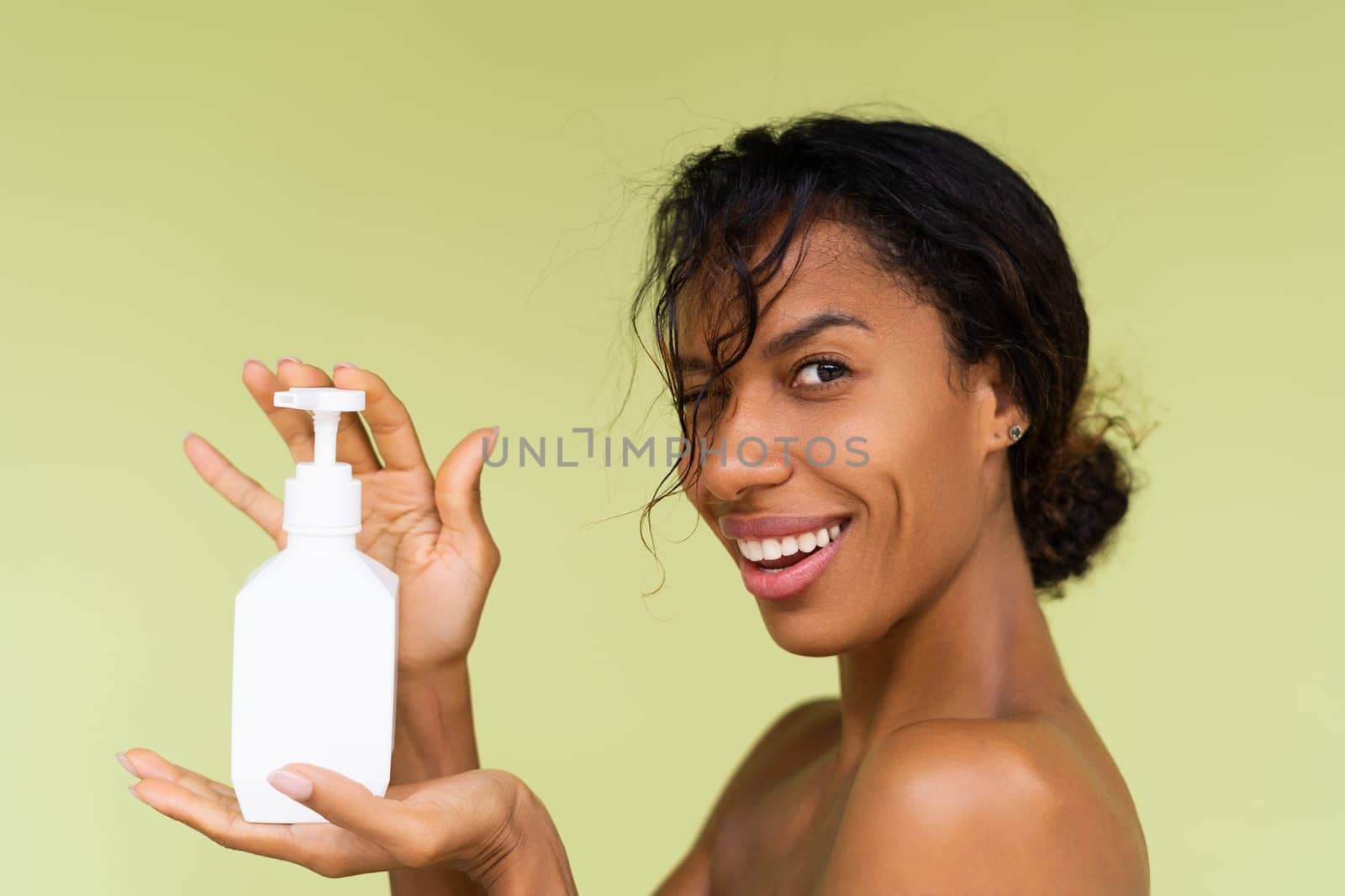 Beauty portrait of young topless african american woman with bare shoulders on green background with white bottle of body lotion by kroshka_nastya