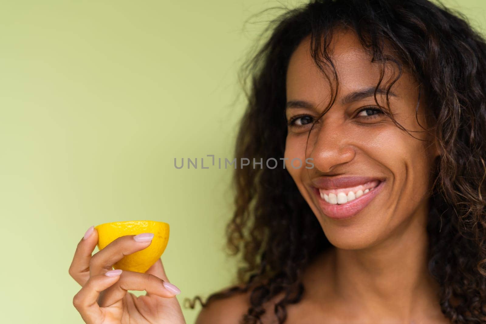 Beauty portrait of young topless woman with bare shoulders on green background with perfect skin and natural makeup holds citrus lemons