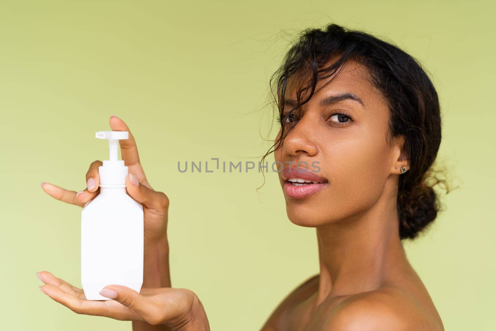 Beauty portrait of young topless african american woman with bare shoulders on green background with white bottle of body lotion by kroshka_nastya