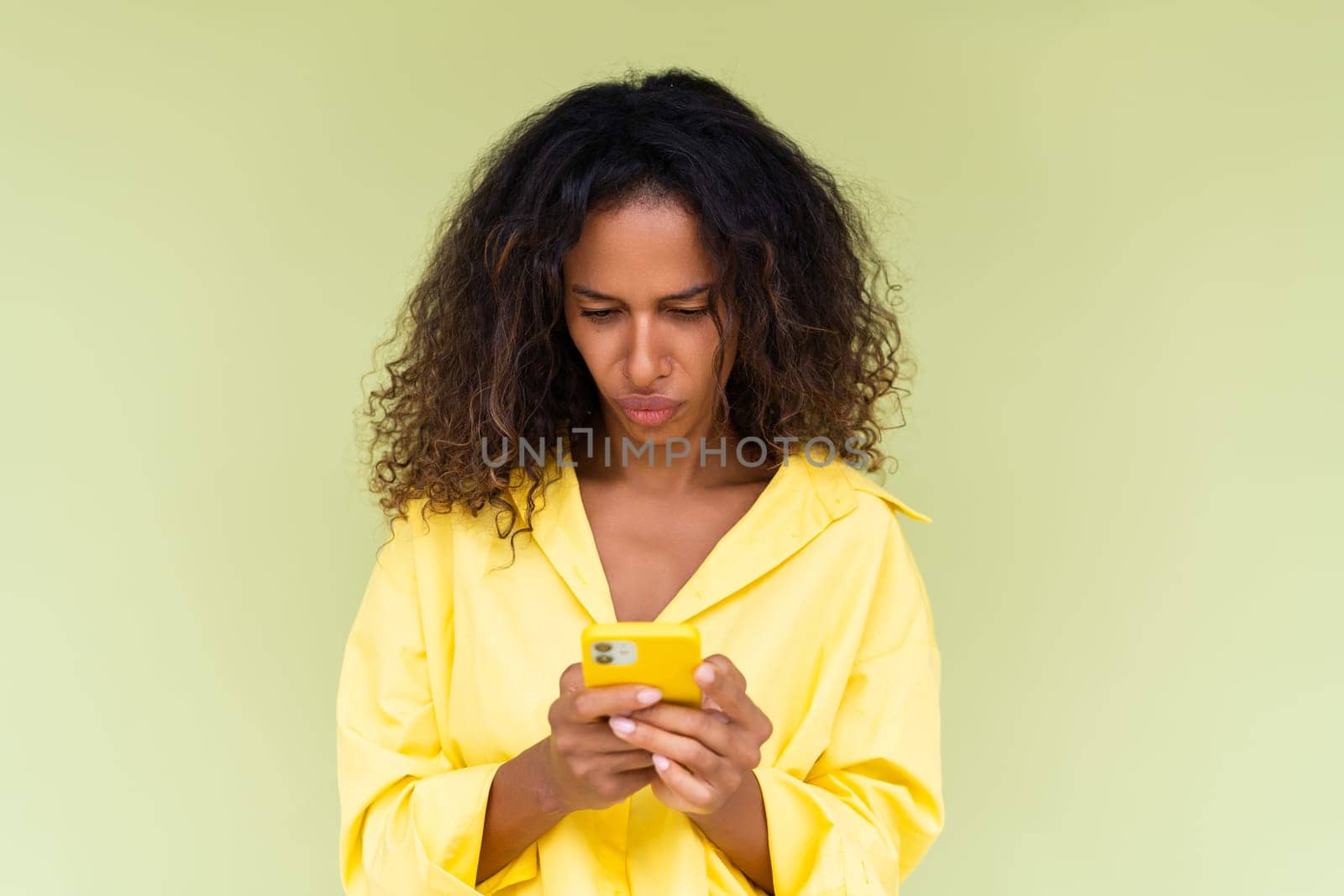 Beautiful african american woman in casual shirt on green background holds a phone confused thoughtful by kroshka_nastya