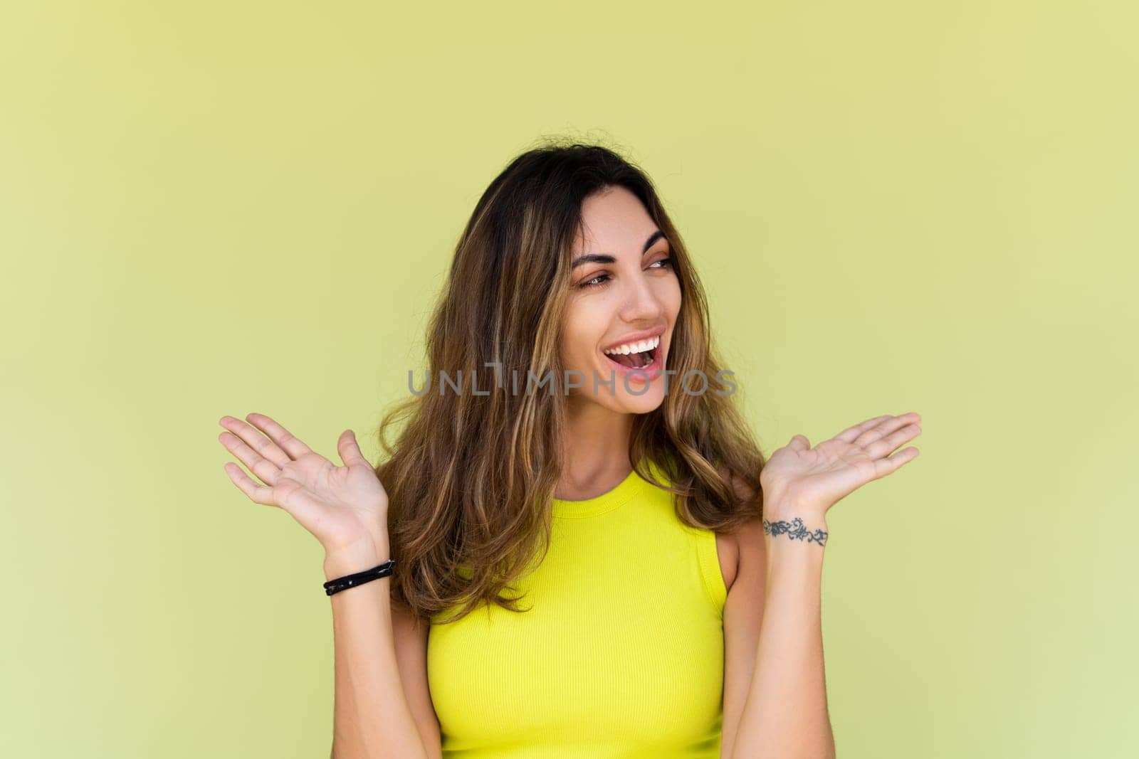 Young brunette in casual wear isolated on green background happy look aside shocked amazed surprised open mouth
