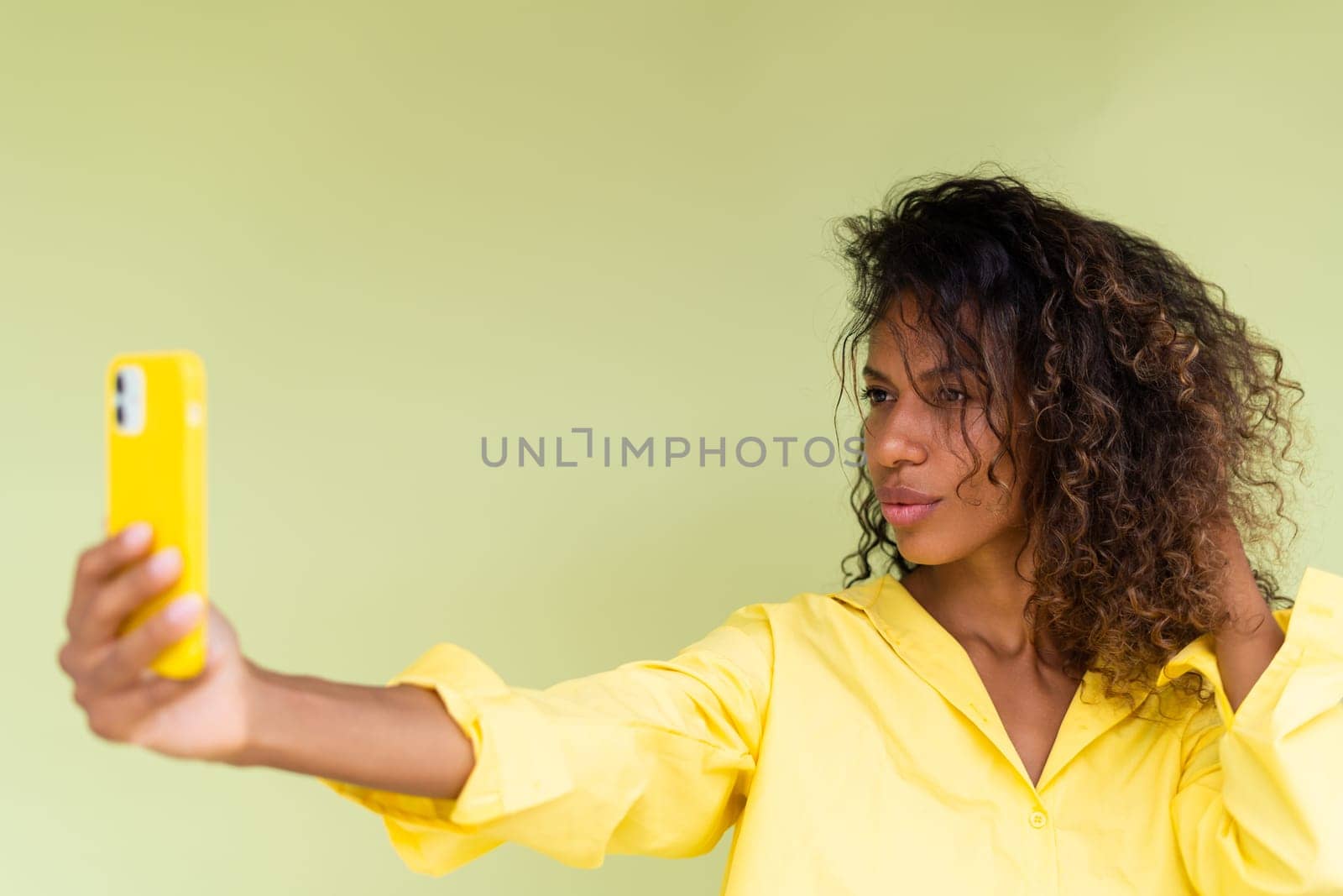 Beautiful african american woman in casual shirt on green background happy taking photo selfie on smart phone by kroshka_nastya