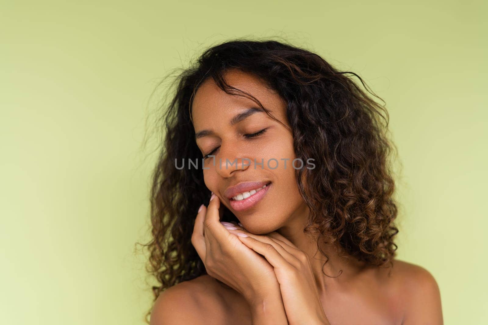 Beauty portrait of young topless african american woman with bare shoulders on green background with perfect skin and natural makeup