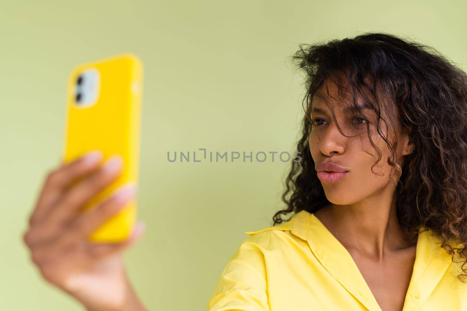 Beautiful african american woman in casual shirt on green background happy taking photo selfie on smart phone
