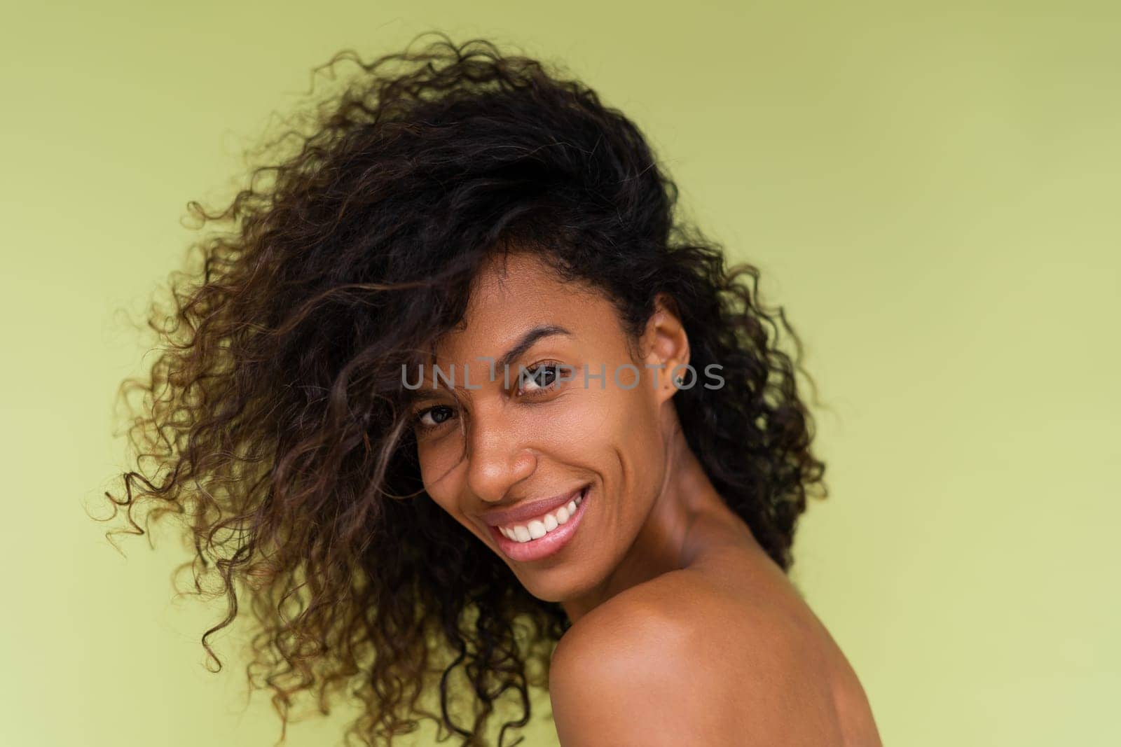 Beauty portrait of young topless african american woman with bare shoulders on green background with perfect skin and natural makeup