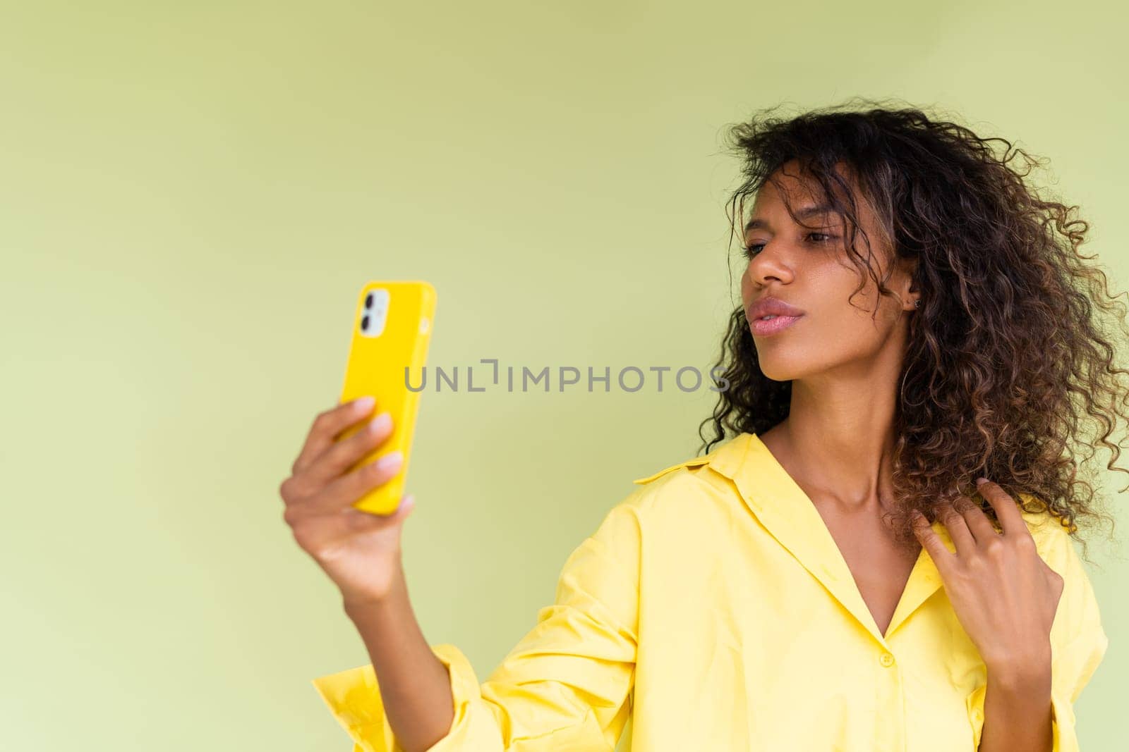 Beautiful african american woman in casual shirt on green background happy taking photo selfie on smart phone