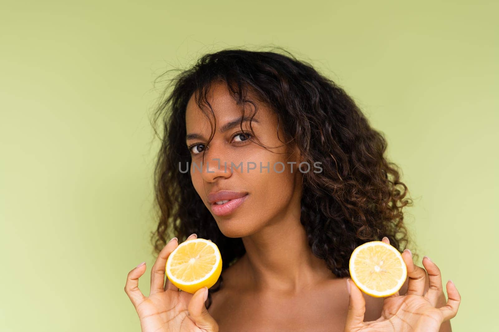 Beauty portrait of young topless woman with bare shoulders on green background with perfect skin and natural makeup holds citrus lemons by kroshka_nastya