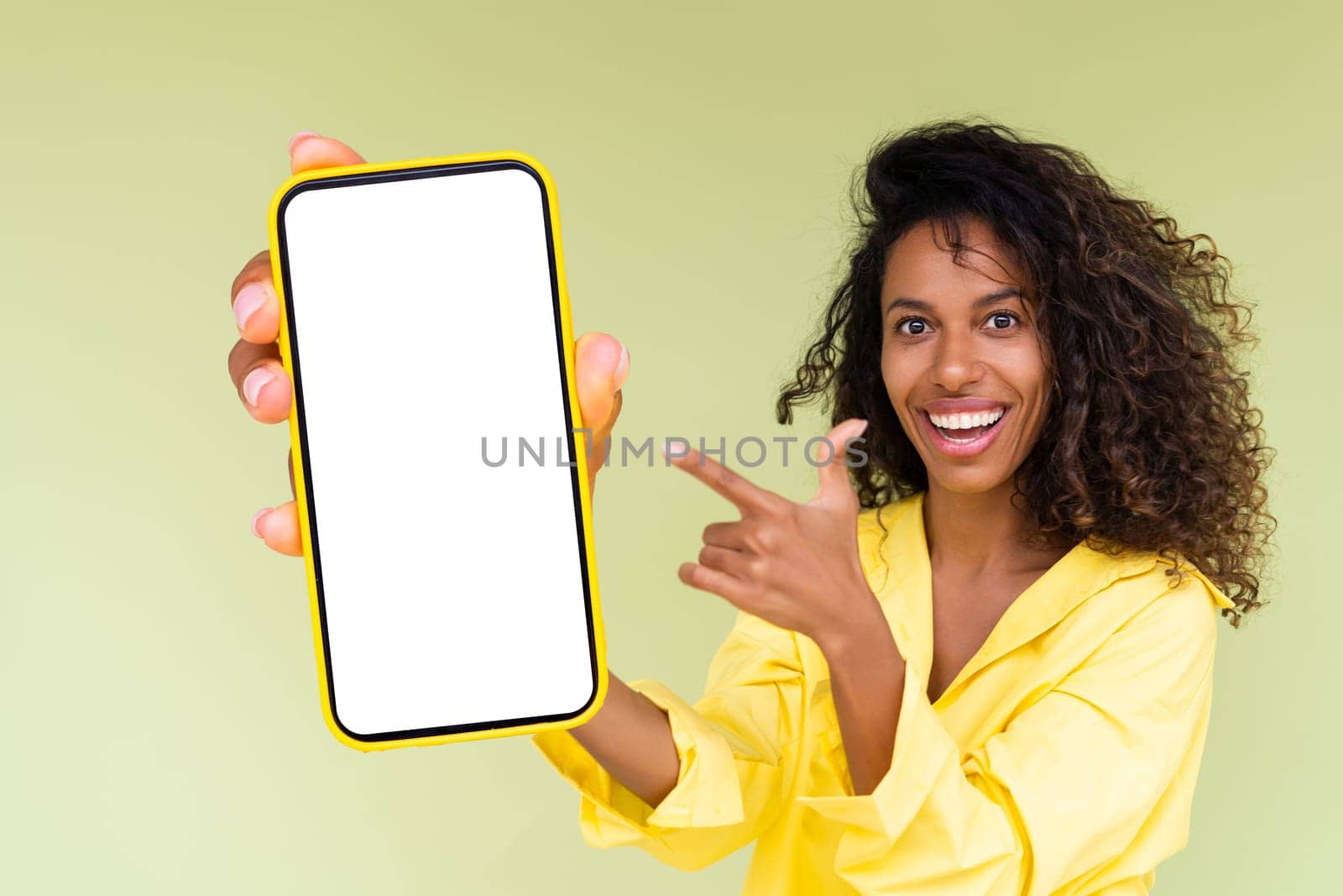 Beautiful african american woman in casual shirt on green background holds a phone with a blank white screen by kroshka_nastya