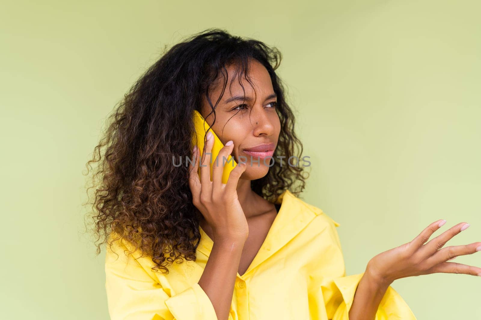 Beautiful african american woman in casual shirt on green background talk on mobile phone shocked confused