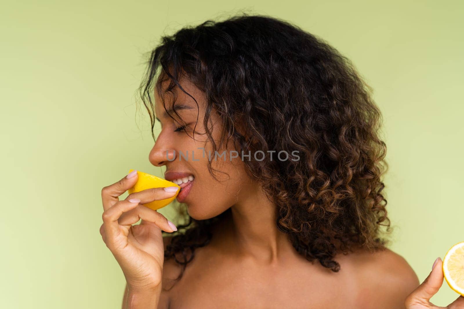 Beauty portrait of young topless woman with bare shoulders on green background with perfect skin and natural makeup holds citrus lemons