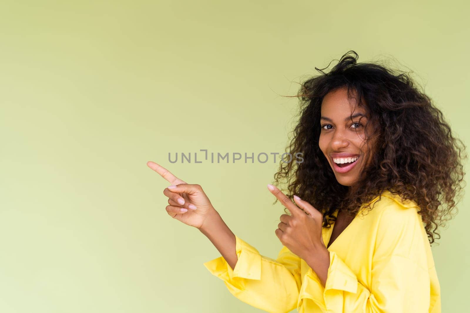 Beautiful african american woman in casual shirt on green background happy positive excited point finger to the left