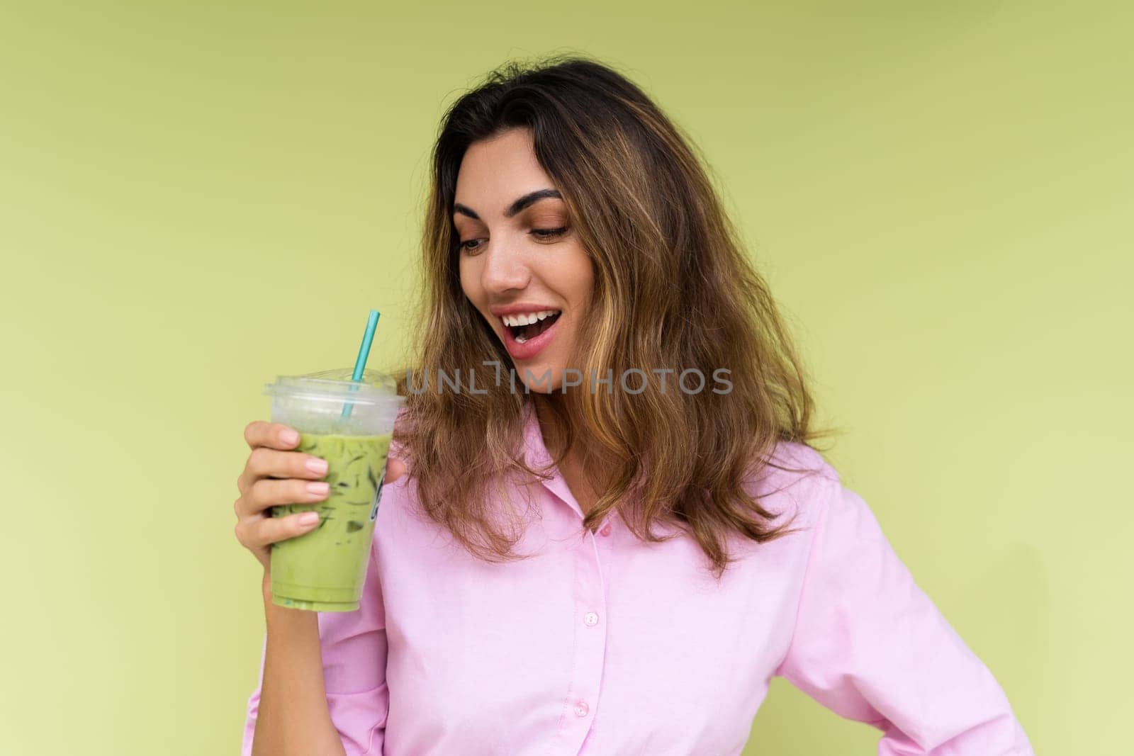 Young woman in casual wear isolated on green background positive vibes enjoying fresh ice green matcha tea with milk at hot summer day by kroshka_nastya